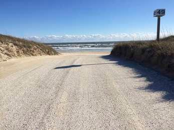 Shell-clay off-road vehicle ramp traversing the dune, with the Atlantic Ocean in the background at a sign painted 