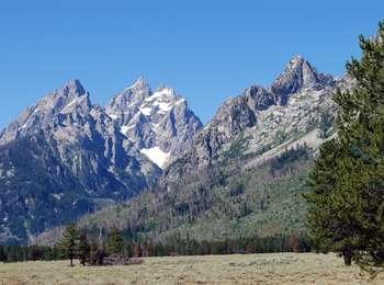 The three peaks of the Cathedral Group - Teewinot, Grand Teton, Mount Owen - to the left of the image. Cascade Canyon and Symmetry Spire to the right. Sagebrush and Lodgepole pines on valley floor.