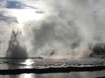 Sunlight behind a geyser erupting into travertine pools