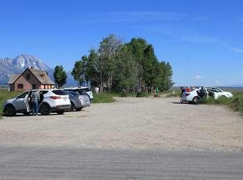 Vehicles parked in the parking lot north of the junction between Antelope Flats and Mormon Row roads. The Pink House and the Teton Range are visible.