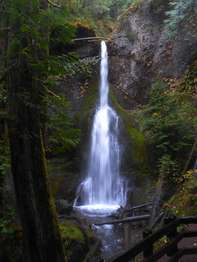 A slender waterfall cascades between moss and stone into a small pool.