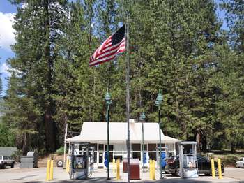 An American flag waves on a flag pole in front of a white building and two gas pumping islands.