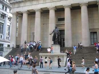 Visitors climb the steps and mingle on the sidewalk in front of the statue of George Washington at Federal Hall.