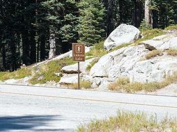 A brown and white roadside sign reads, "Lukens Lake," and has an icon of a hiker.