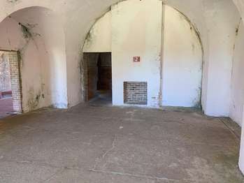 White, plaster lined walls with a small brick opening in the wall. A brown metal sign with the number,