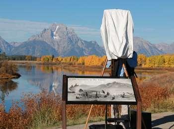 View of Mount Moran reflected in the Oxbow Bend with golden-leafed aspen trees in the middle-ground. A wayside about American Indian culture is in front of a photographer.