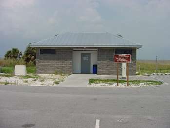 Cement building with one grey metal door in the center. A parking lot in the foreground.