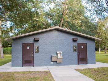 Grey cement building with two brown metal doors. Next to each door is a men's and women's restroom symbol sign.