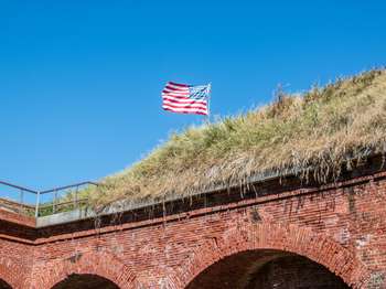 Brick scarp wall supporting a grassy mound. An American flag peeks over the top of the mound.