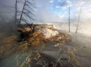 Steam rises above orange and rust-colored terraces with pools of blue water.