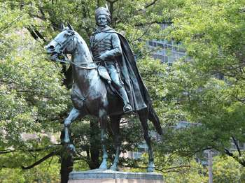 A bronze state of a man riding a horse. The man wears a long cape and tall, furry cap. 