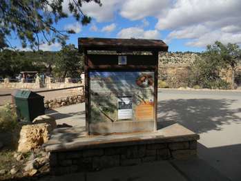 A wood and metal sign with wooden cover and a stone base displays a graphic and text describing the local source of a spring on the north side of the canyon. 