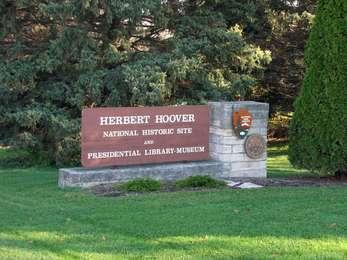 A large brown roadside sign with white letters and a stone foundation announces a park entrance.