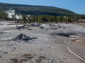 Rubble in an open area with puffs of steam emerging from a forested hillside