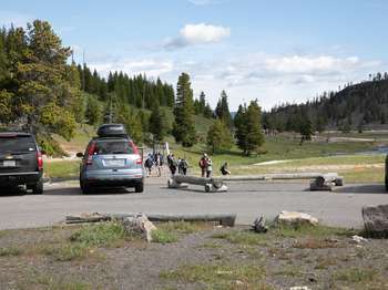 Cars are parked in the paved parking lot and visitors walk along the trail.