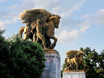 Two golden statues of men walking alongside winged horses.