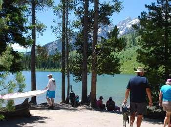 Visitors picnicking on lake shore and carrying boat to water.