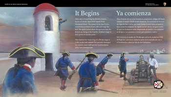 A full color illustration fills the entire panel. At the left, a tall white rounded belltower with a bell hanging from a wooden beam under a red roof is on the corner of the fort. Beyond the tower is a blue-grey and muted orange sky and next to the fort is the pale blue shore of a river. Inside the tower, a soldier in a blue uniform leans out of one of the  high rounded vertical window openings; his left arm and hand extends outward towards  soldiers below.  Below, to the right 5 soldiers in blue uniforms with red trim at the neck and wrists and black tri cornered hats actively respond to the soldier in the tower. 2 soldiers move forward with long brown muskets; a third soldier holds a long brown cannon ram rod and leans toward a cannon set on a low, 4-wheeled cart. The fifth soldier points toward enemy ships. To the right of the cannon a man in a white shirt and blue breeches adjusts the cannon and looks out towards the water. In the distance, smoke appears from points on Anastasia Island and four, 2-masted ships with white sails   At the upper center and right of the panel, white text in English and Spanish reads:  It Begins. After days of watching the British prepare, bursts of smoke signal their attack from Anastasia Island. The sentry in the San Carlos watchtower in front of you yells and rings the bell. His quick action alerts the garrison that the British are firing at the Castillo. Soldiers surge to their posts or run for cover.  This marked the beginning of a 38-day siege in 1740. In the end, cannon fire partially damaged the eastern outer wall and the bombardment killed 2 townspeople.  End of Text  At the bottom right, a small circle divided into 4, triangular wedges. Each wedge has a portion of a flag and date range for an important period in the fort's history. 1 wedge is bright, indicating the time period of the panel story and the other three wedges are muted. From the top, moving clockwise: Great Britain: 1763-1784; Spain: 1784 to 1821; the United States: 1821-1900; and Spain: 1672-1763, is bright.  Below the circle, light grey text in English and Spanish reads: First Spanish Military Era.  Immediately to the left of the panel, a low stone wall extends ahead toward the fortâ€™s v-shaped corner and its rounded, 2-story bell tower. On this level, is a rectangular doorway; above on all 4 sides, tall, rounded openings. Ahead and to the right of the bell tower is a wooden platform with three reproduction cannons.  Beyond the walls, views of the Matanzas River and the tops of palm trees.  [End of Message]