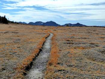 A trail through a flat area, with mountains in the distance.
