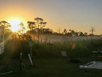 Campsite in early morning mist. Sunburst over trees in the background.