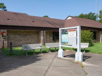 Metal framed National Park Service signs on a small structure. Park headquarters brick building in the background.