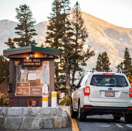 A female park ranger assists a person in a car at a park entrance kiosk.