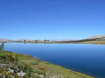 A chain of mountains can be seen at the far end of a large body of water. The upper half of the photo is a clear blue sky.
