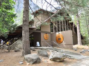 A brown, A-frame building is surrounded by trees and has two circular signs on the side of the building. One sign reads, The Loft at Degnan's, and the other sign reads Degnan's Kitchen.