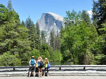 Three people stand on a bridge looking at Half Dome.