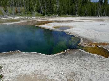 A deep, steaming pool with a runoff channel lined by orange and white.