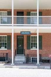 This image shows the entrance to the John Brown Museum. It is a large, brick building with a dark green door and windows with white beams and a balcony.