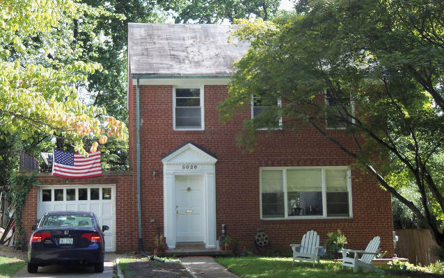 Two story brick house with an American flag surrounded by trees