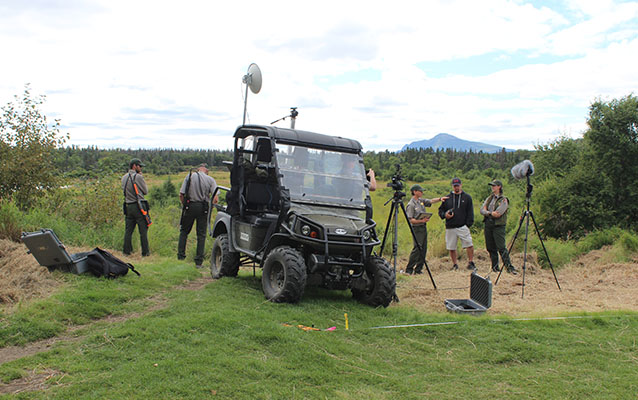 NPS staff are filming work near grass covered archeological house ruins at Brooks River NHL.