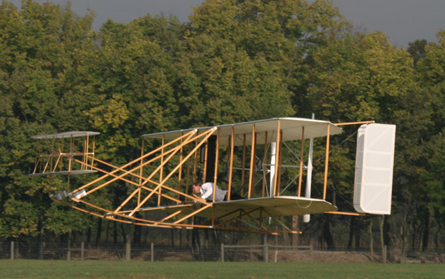 A replica Wright brothers plane hovers feel above the grass-covered ground A replica Wright brothers plane hovers feel above the grass-covered ground