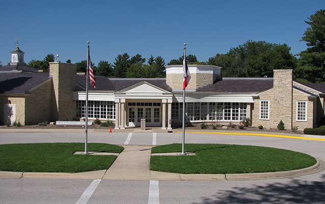 A sprawling one story public building of rough-faced yellowish stone has a white portico entrance. A sprawling one story public building of rough-faced yellowish stone has a white portico entrance.