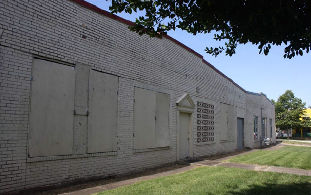 One story white brick commercial building with boarded up windows