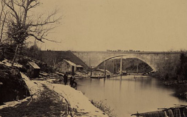 Union Bridge in the distance circa 1863. Two people in the foreground looking at camera. Union Bridge in the distance circa 1863. Two people in the foreground looking at camera.