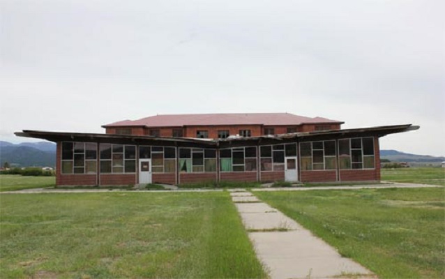 Front view of the building with its sloping roof. Grass and walkway in the foreground.