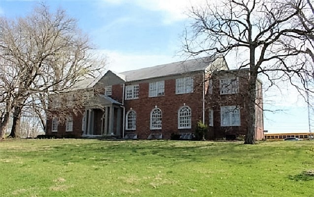 a large house on a hilltop, flanked by two tall, bare-limbed trees