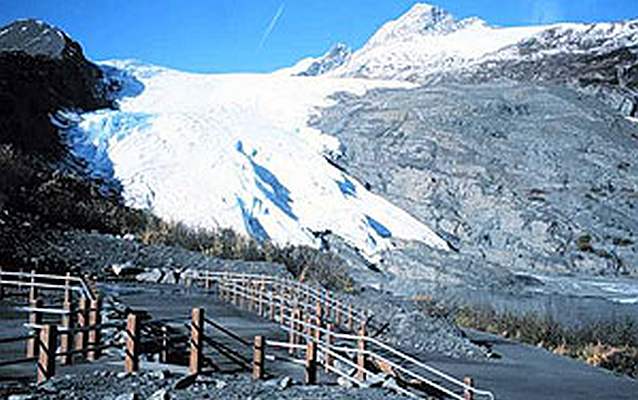 a view of a glacier with a paved path and fence in the foreground