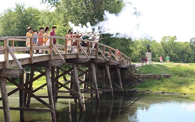 Living history reenactors fire muskets from the wooden North Bridge in Concord, MA