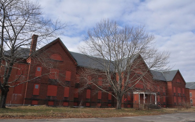 Exterior of a red brick building with boarded up windows.
