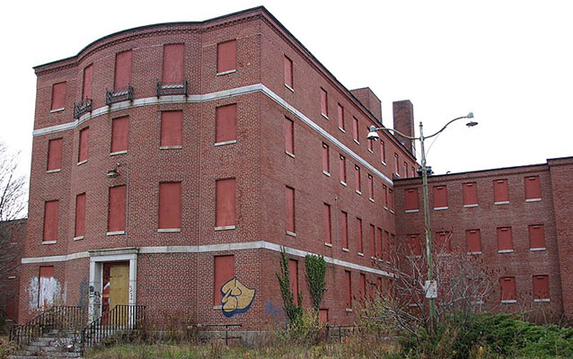 Exterior of a four story red brick building with boarded up windows.