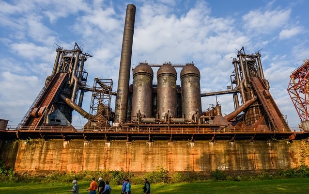 People walk on grass next to the Carrie Blast Furnaces. People walk on grass next to the Carrie Blast Furnaces.