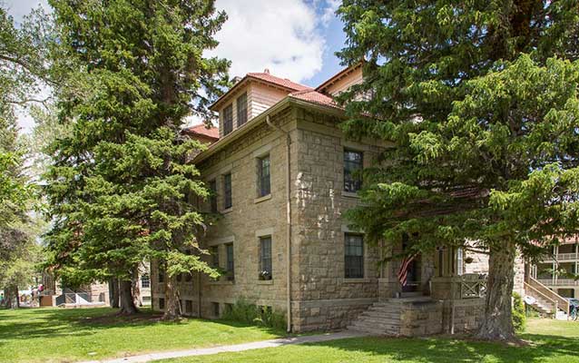 Front of the large stone building, surrounded by tall pine trees. Front of the large stone building, surrounded by tall pine trees.