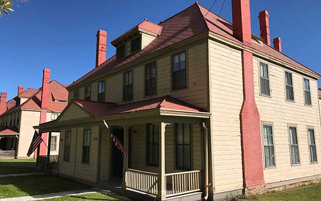 Tan wooden house with red brick chimneys and red tin roof.