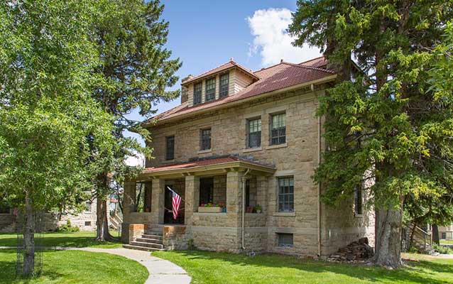 Front of the large stone building, surrounded by tall trees.