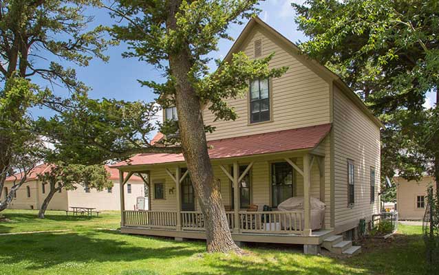 Tan wooden house with porch and red tin roof.