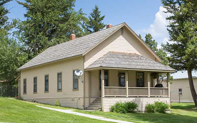 Tan wooden house with porch and wooden shake roof.