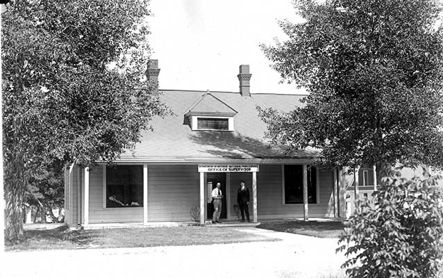 Black-and-white photograph of the single-story wooden building with two men standing out front.